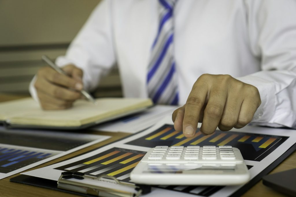 An Asian male finance worker uses a calculator to calculate corporate tax expenses after deducting p