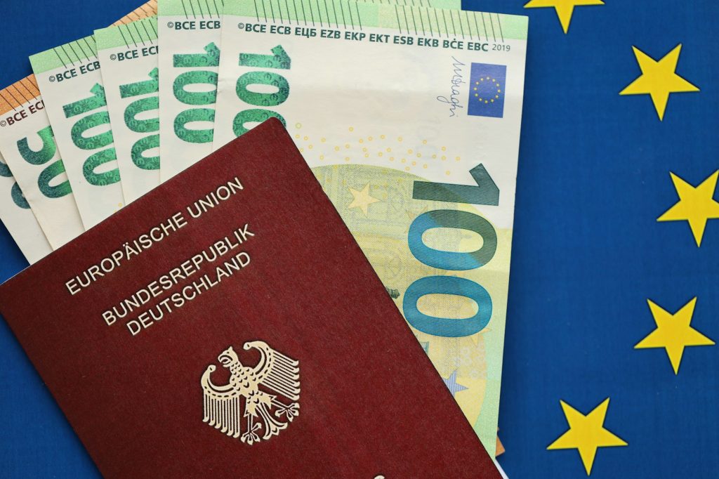 Red German passport of European Union and money on blue flag background close up